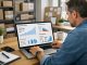 How a Small Business Can Leverage AI to Lower Costs and Scale in 2026 A man in a casual shirt analyzes sales performance graphs on a laptop in an office. The workspace is organized and focused, with charts showing upward trends.