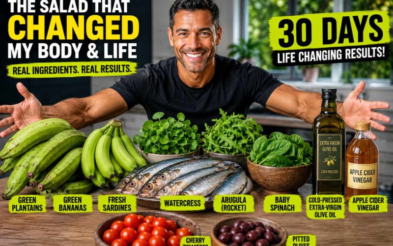 Fit, healthy mixed-race man smiling with his arms outstretched over a table filled with green plantains, green bananas, fresh sardines, watercress, arugula, baby spinach, extra-virgin olive oil, apple cider vinegar, cherry tomatoes, and pitted olives in a bright modern kitchen, showcasing the fresh ingredients used in a nutrient-dense sardine and green plantain salad.